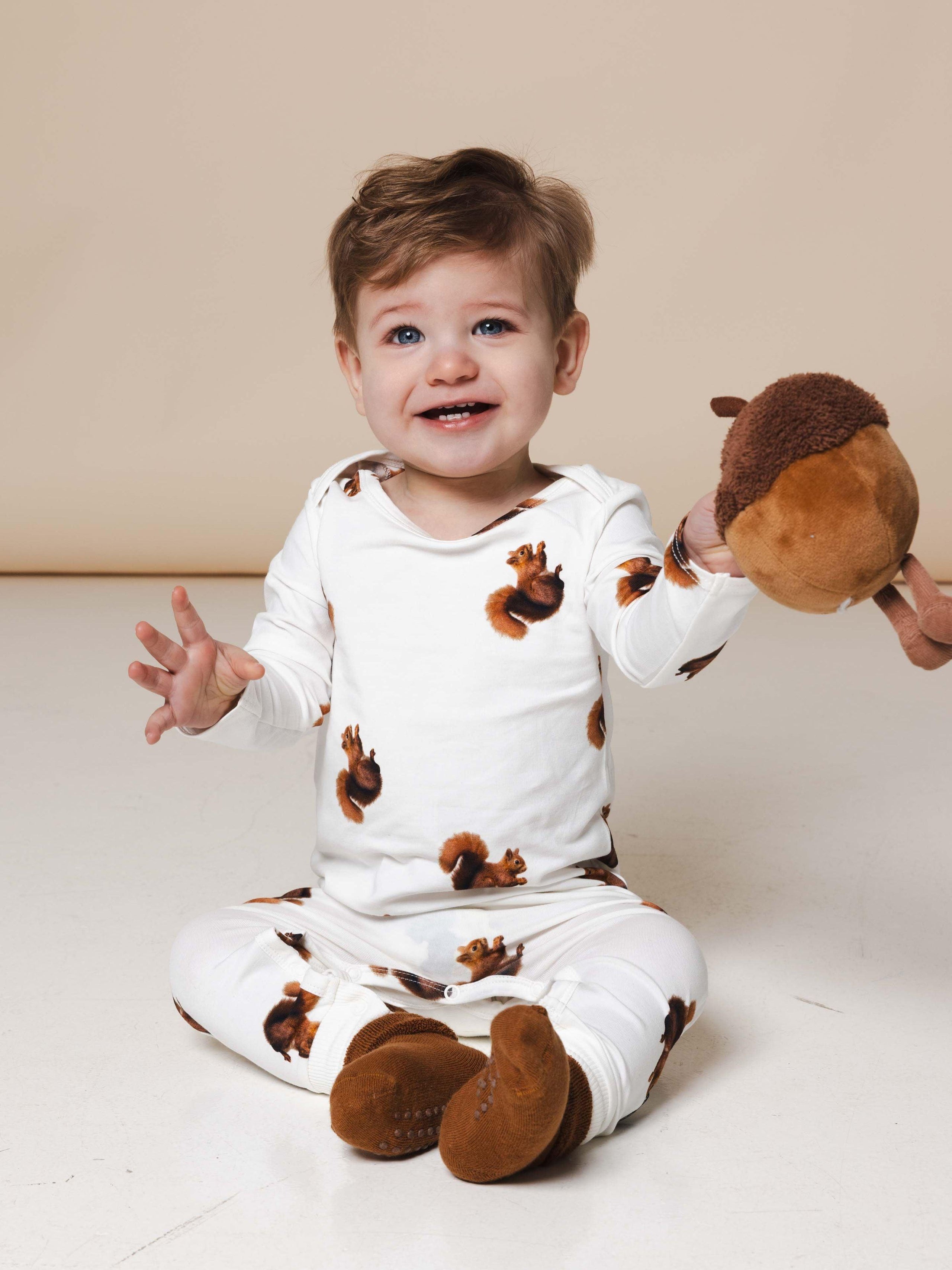 Baby wearing a squirrel print jumpsuit holding an acorn plushie